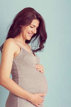 Portrait of happy pregnant woman with hands on belly isolated over blue background