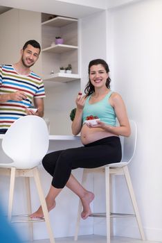 young pregnant couple eating strawberries at kitchen, lifestyle healthy pregnancy happy life concept