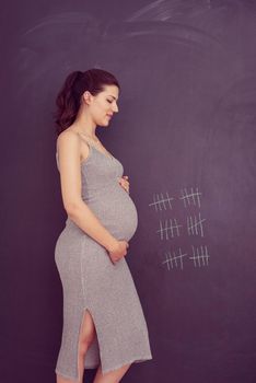 Portrait of happy pregnant woman with hands on belly in front of black chalkboard