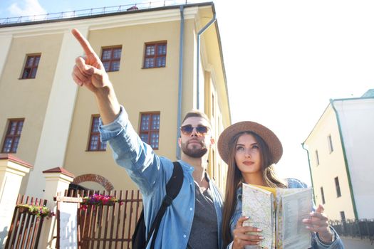 Happy couple walking outdoors sightseeing and holding a map.