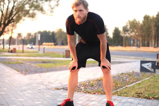 Handsome young man after run resting after jog at the park at sunset or sunrise