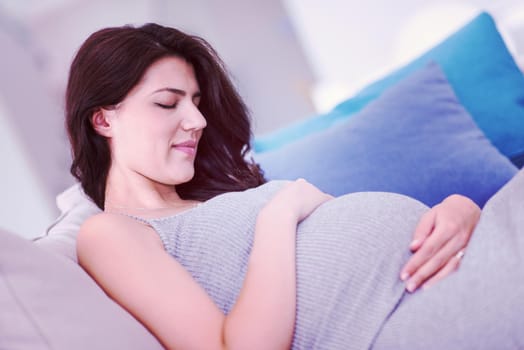 young happy pregnant woman keeping hand on belly while sitting on sofa at home