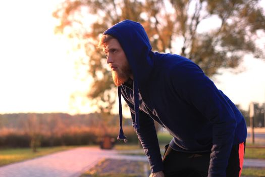 Handsome young man after run resting after jog at the park at sunset or sunrise