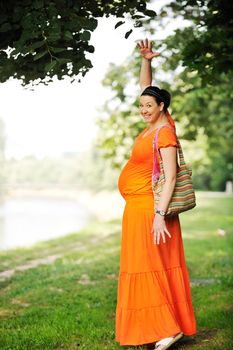 beautiful young happy pregnant woman outdoor in bright nature in orange dress