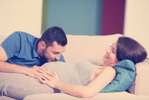 Happy future dad listening the belly of his pregnant wife while relaxing on sofa at home