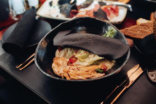 Contemporary cuisine with served Caesar salad with chicken in black bowl covered with black slice with sesame seeds.