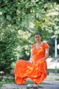 beautiful young happy pregnant woman outdoor in bright nature in orange dress