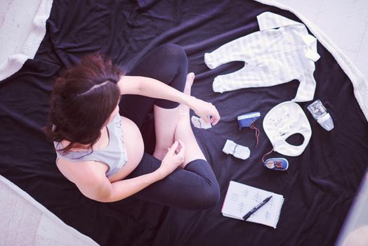 a pregnant woman at home on the floor checking list of baby clothes preparing for going to maternity hospital top view.Pregnancy, birth concept