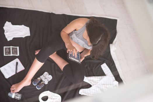 a pregnant woman at home on the floor checking list of baby clothes preparing for going to maternity hospital top view.Pregnancy, birth concept