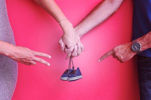 young  pregnant couple holding newborn baby shoes isolated on red background,family and parenthood concept