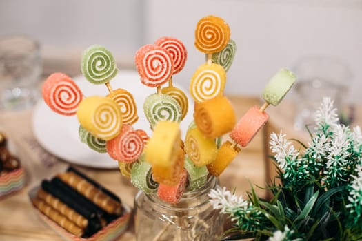 Sweet colorful fruit candies with sugar and natural juice on wooden sticks in glass jar at candy bar.