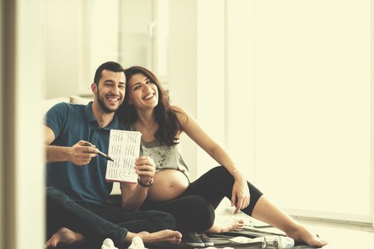 a happy pregnant couple checking a list of things for their unborn baby at home on the floor