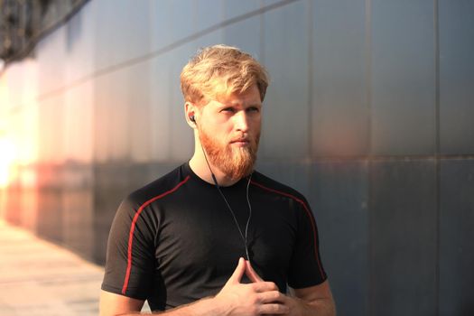 confident sporty young man with crossed arms looking at camera while standing outside, at sunset or sunrise. Runner.