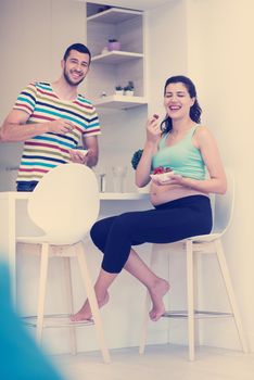 young pregnant couple eating strawberries at kitchen, lifestyle healthy pregnancy happy life concept