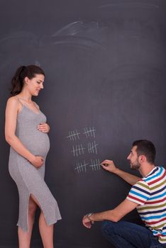 young pregnant couple accounts week of pregnancy and writing them with chalk on blackboard