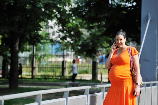 BEAUTIFUL YOUNG PREGNANT WOMAN WALKING OUTDOOR AND TAKING ON CELLPHONE