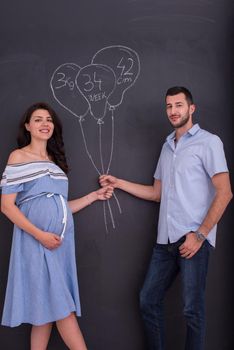 Conceptual photo of pregnant couple drawing their imaginations about the future life with children on chalk board