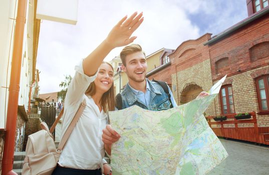 Happy couple walking outdoors sightseeing and holding a map.