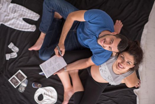 top view of a happy pregnant couple checking a list of things for their unborn baby at home on the floor