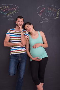 young pregnant couple thinking about names for their unborn baby and writing them on a black chalkboard