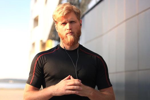 confident sporty young man with crossed arms looking at camera while standing outside, at sunset or sunrise. Runner.