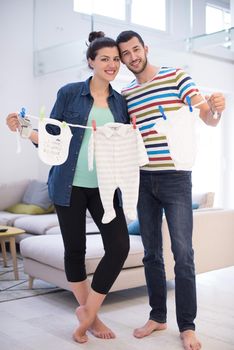 Beautiful pregnant woman and her husband expecting baby holding baby bodysuits and smiling at home