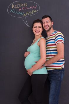 young pregnant couple thinking about names for their unborn baby and writing them on a black chalkboard