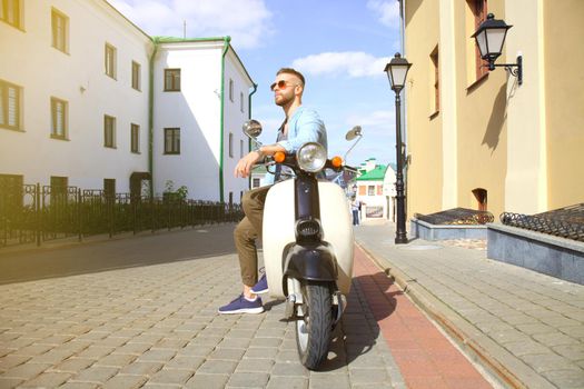 Cheerful young man is riding on scooter in town.