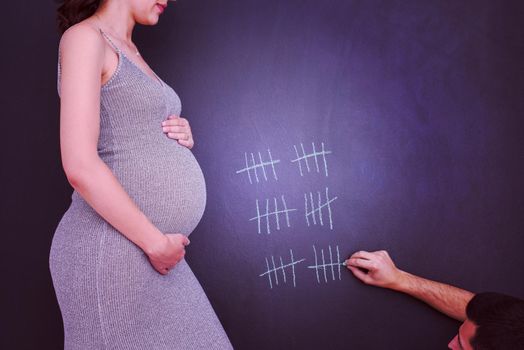 young pregnant couple accounts week of pregnancy and writing them with chalk on blackboard