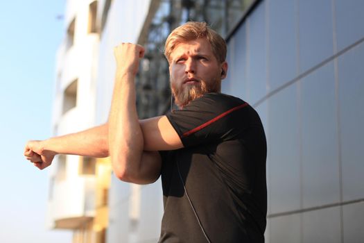 Handsome young man doing stretching exercises before running while standing outdoors