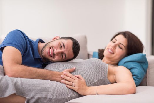 Happy future dad listening the belly of his pregnant wife while relaxing on sofa at home