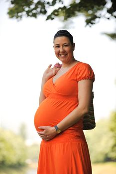 beautiful young happy pregnant woman outdoor in bright nature in orange dress