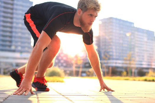 Sporty young man in start position outdoor at sunset or sunrise