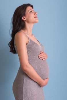 Portrait of happy pregnant woman with hands on belly isolated over blue background