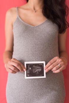 smiling pregnant woman showing ultrasound picture of her unborn baby isolated on red background