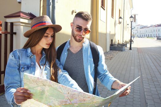 Happy couple walking outdoors sightseeing and holding a map.