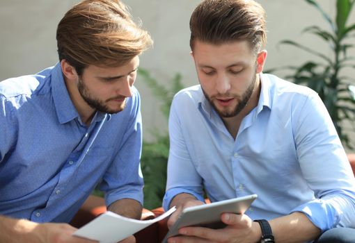 Mature businessman using a digital tablet to discuss information with a younger colleague in a modern business office