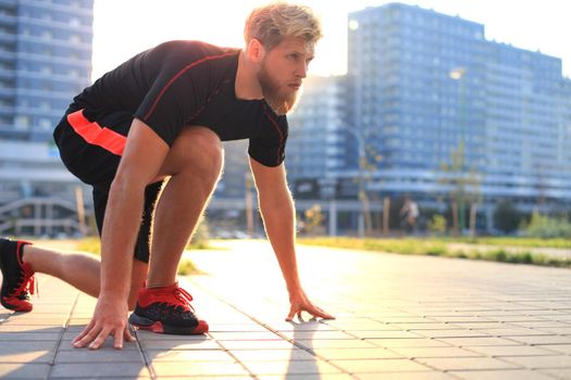 Sporty young man in start position outdoor at sunset or sunrise