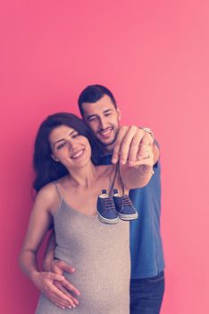 young  pregnant couple holding newborn baby shoes isolated on red background,family and parenthood concept