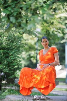 beautiful young happy pregnant woman outdoor in bright nature in orange dress