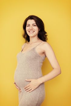 Portrait of happy pregnant woman with hands on belly isolated over yellow background