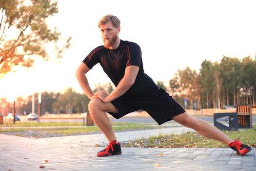 Handsome young man doing stretching exercises before running while standing outdoors