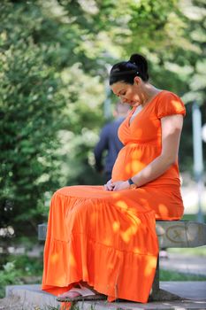 beautiful young happy pregnant woman outdoor in bright nature in orange dress