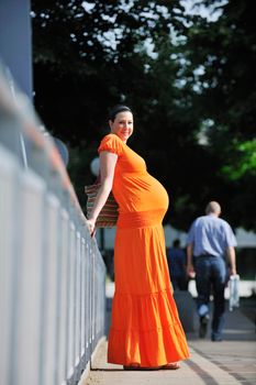 beautiful young happy pregnant woman outdoor in bright nature in orange dress