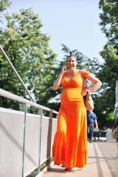 BEAUTIFUL YOUNG PREGNANT WOMAN WALKING OUTDOOR AND TAKING ON CELLPHONE