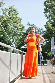 BEAUTIFUL YOUNG PREGNANT WOMAN WALKING OUTDOOR AND TAKING ON CELLPHONE