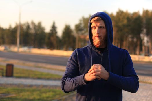 confident sporty young man with crossed arms while standing outside, at sunset or sunrise. Runner.