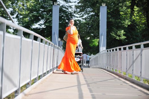 BEAUTIFUL YOUNG PREGNANT WOMAN WALKING OUTDOOR AND TAKING ON CELLPHONE