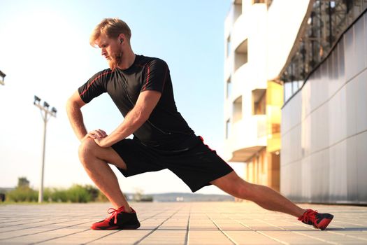 Handsome young man doing stretching exercises before running while standing outdoors