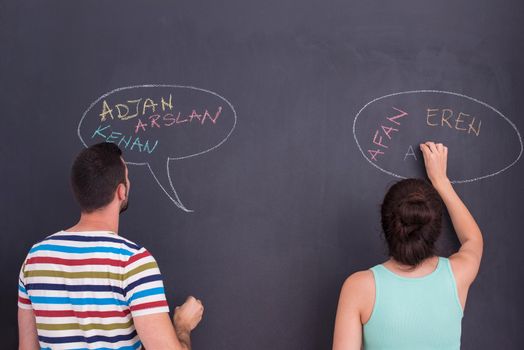 young pregnant couple thinking about names for their unborn baby and writing them on a black chalkboard